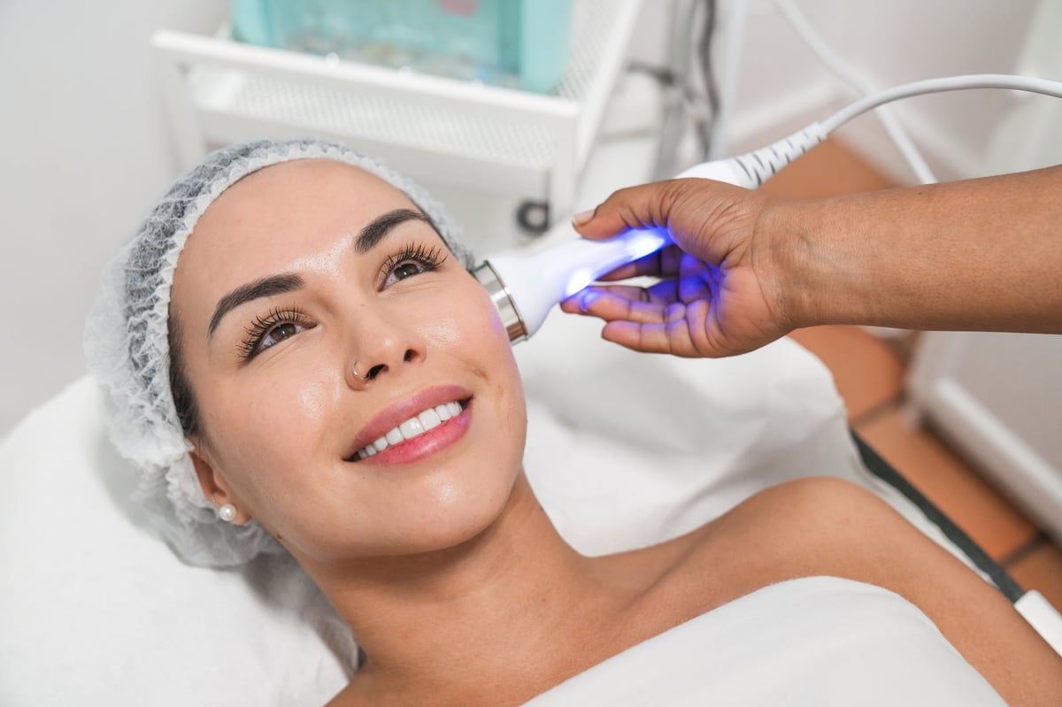 Beautician applying a modern skin treatment on a smiling woman's face inside a bright beauty studio