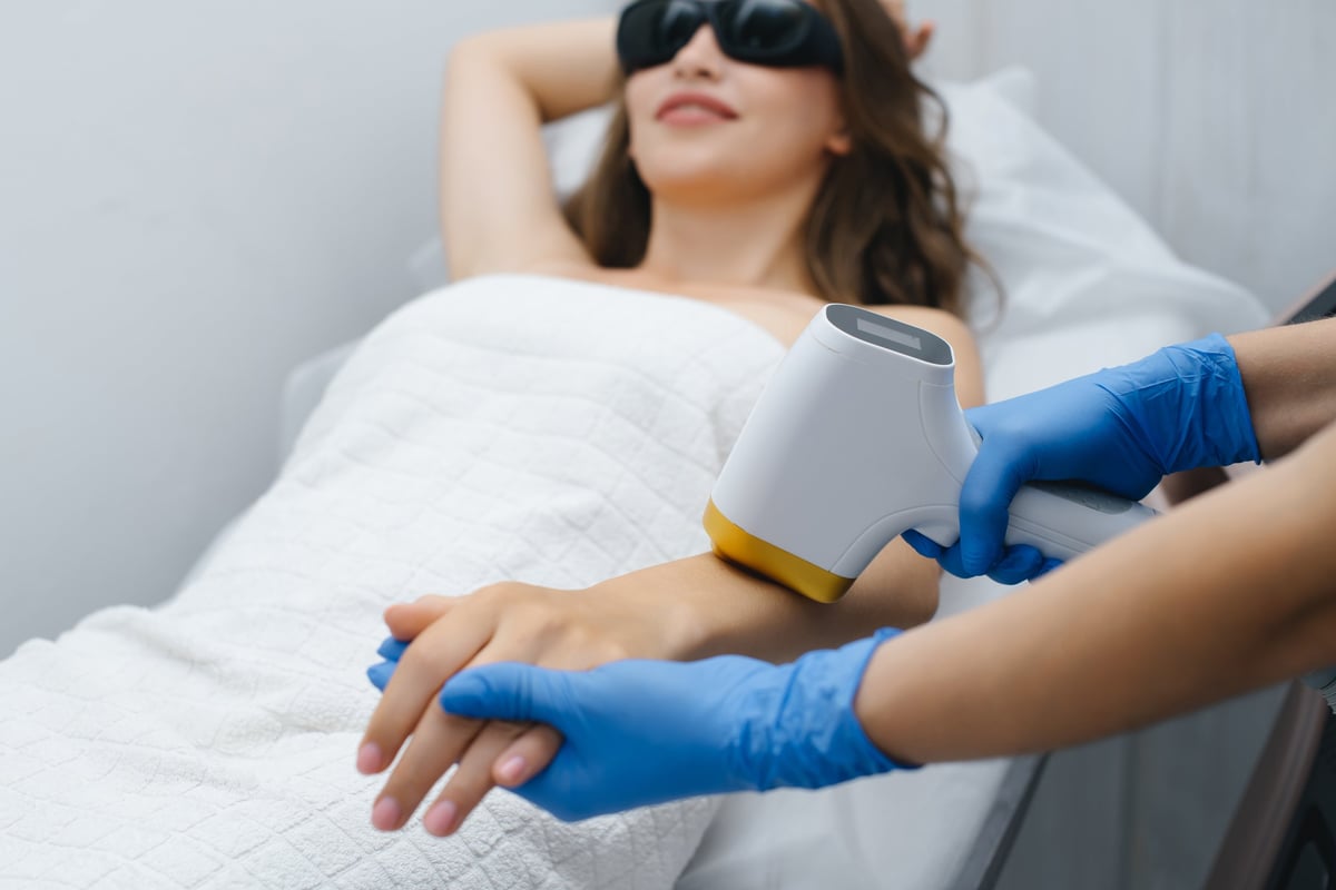 laser epilation, hair removal procedure, young beautiful caucasian smiling brunette woman lying on couch in beauty salon, arm epilation, spa and cosmetology concept