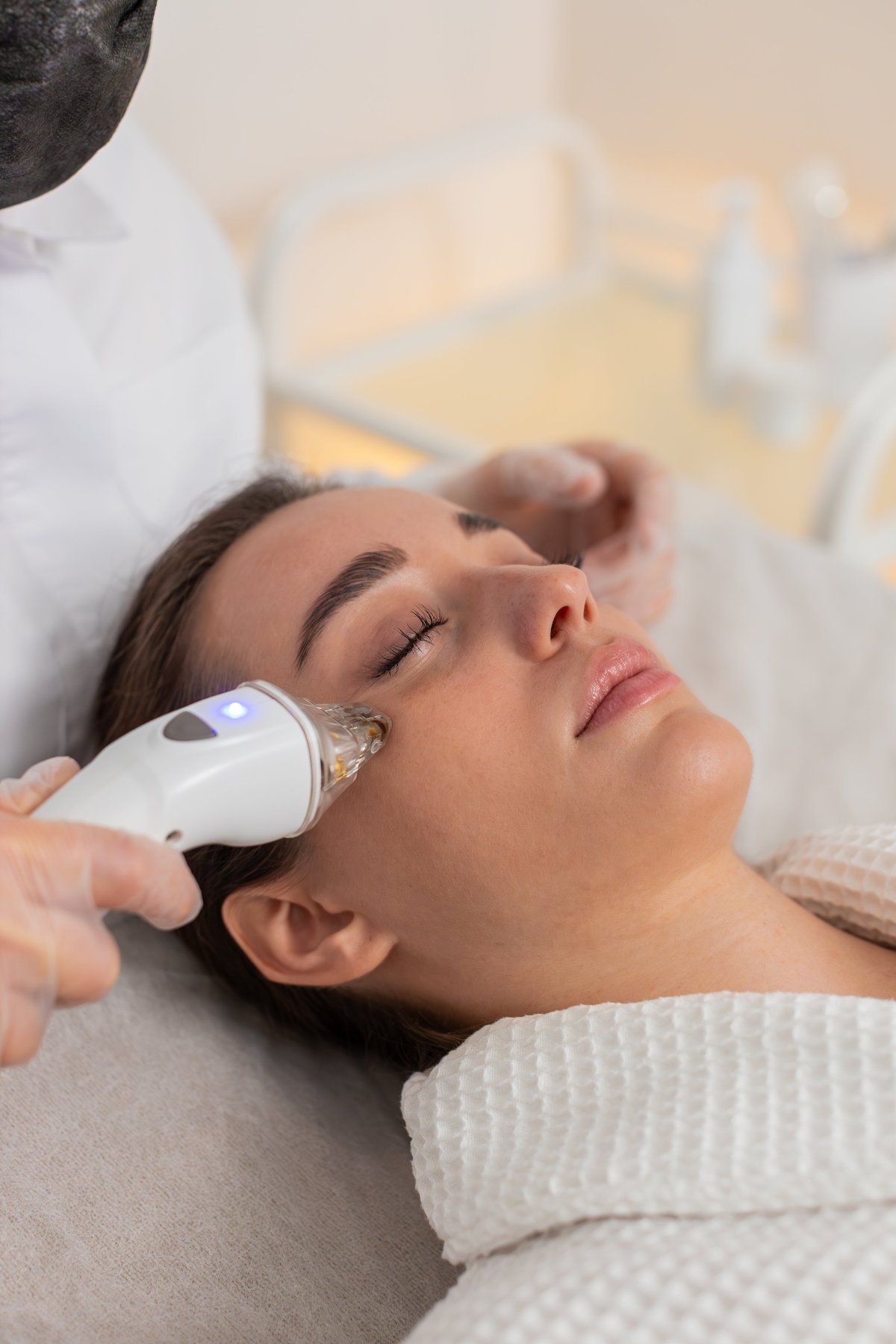 Caucasian woman receives gentle skin treatment in a modern cosmetology studio while a specialist explains the skin analysis