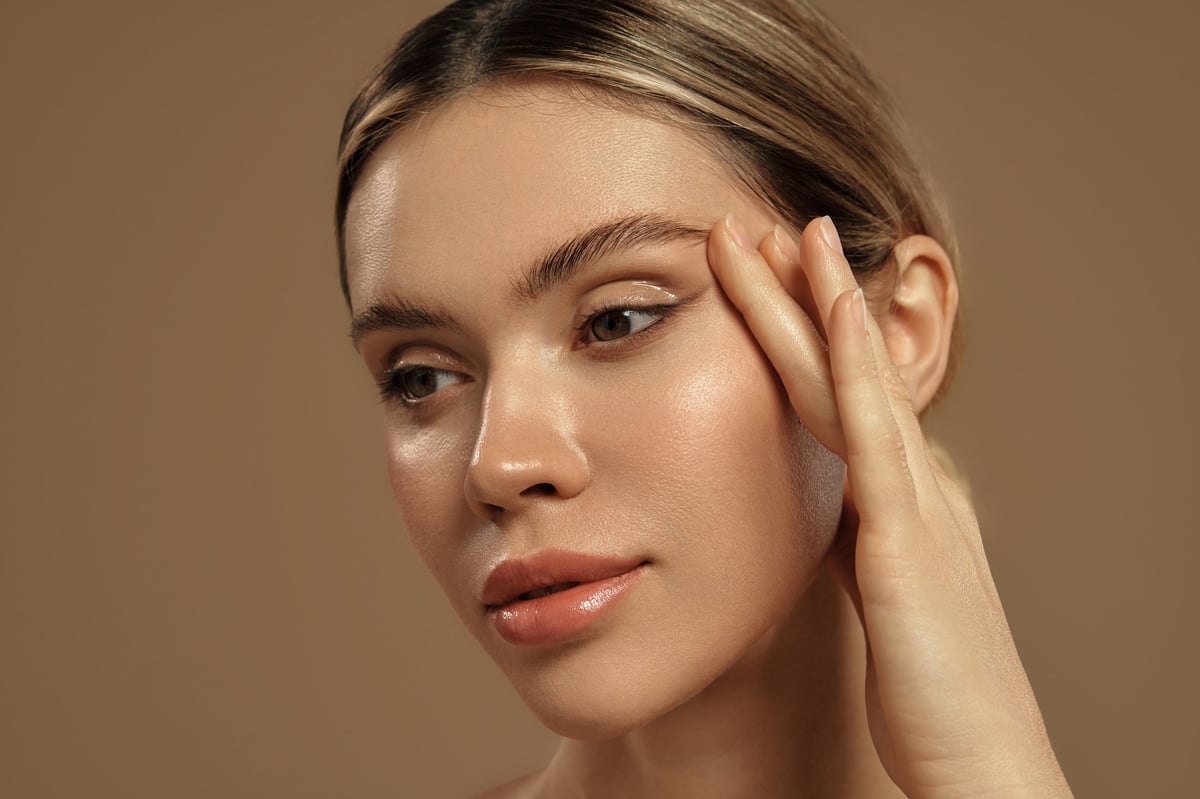 Portrait of a young woman with glowing skin gently touching her face. Natural makeup and healthy skincare concept.