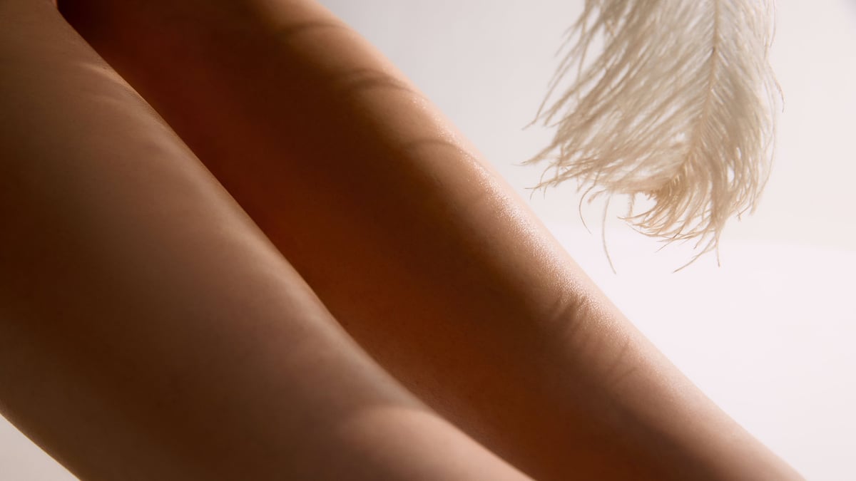 Close abstract view of smooth female legs with soft feather motion in warm background. Concept of aesthetic dermatology, laser prep visuals, cosmetic skin treatment and feminine care.